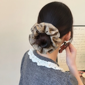 Gros plan d'un chouchou à carreaux kaki sur un chignon, accessoire cheveux élégant