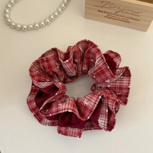 Close-up of a red and white plaid scrunchie with bow patterns and elegant pearl decor