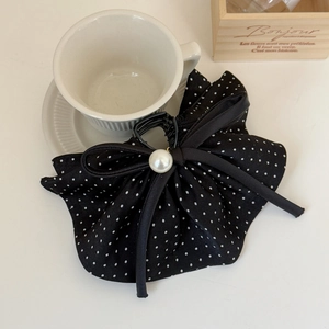 Elegant polka dot bow hair claw with central pearl on a minimalist white desk
