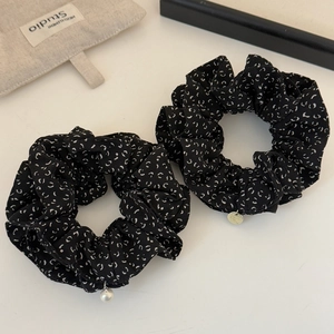 Détail de deux chouchous noirs à motifs de lune avec une perle et un pendentif métallique