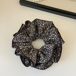 Detail of floral scrunchie with blue and white flowers on dark brown fabric background