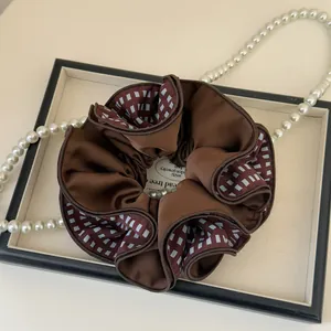 Detailed shot of dark brown satin scrunchie with grey checkered trim on display tray