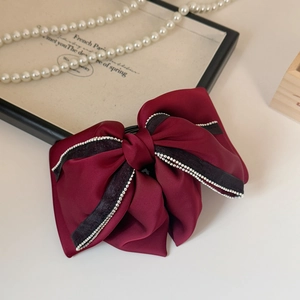 Detailed close-up of a burgundy silk bow hair claw clip with elegant silver bead trim decor