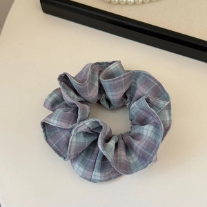 Détail d'un chouchou à carreaux avec plis en tissu bleu et violet sur surface blanche