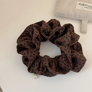 Détail d'un chouchou large à motif léopard avec un pendentif décoratif en perle blanche