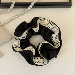 Dettaglio di uno scrunchie in raso nero con bordo in pizzo bianco in stile vintage francese