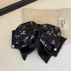 Dettaglio della molletta per capelli a fiocco nero floreale con perle e texture in chiffon