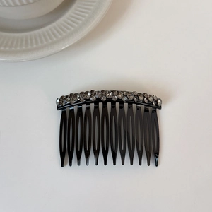 Detail of a curved black hair comb with luxury dark grey rhinestones on a white surface