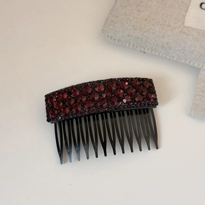 Macro detail of wine red crystals on a black curved hair comb accessory for women