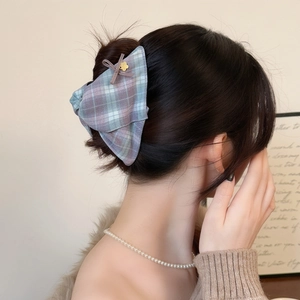 Close-up of British style plaid bow hair claw with gold flower detail on model