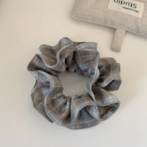 Detailed view of brown and light blue plaid checkered scrunchie on a minimalist surface