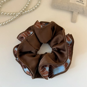 Close-up of silk satin scrunchie featuring elegant brown and blue floral double-sided pattern