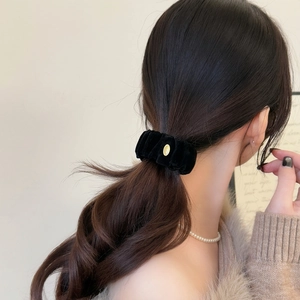 Détail d'un chouchou en velours noir avec boucle dorée sur une coiffure en queue de cheval