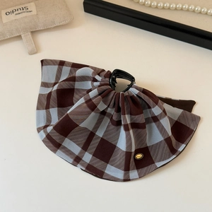 Detail of a brown and blue plaid fabric bow hair claw clip with golden metal emblem