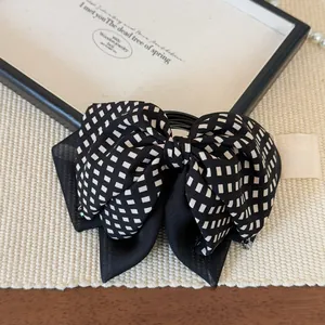 Detail view of checkered bow hair tie with dual-layer fabric on a textured surface