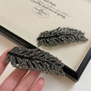 Close-up of sparkling black rhinestone leaf hairpin held in hand for detail display