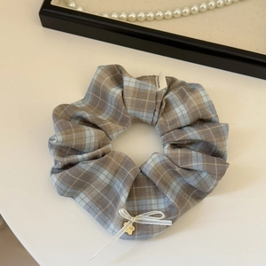 Detail of grey-blue plaid scrunchie with white ribbon bow and gold flower pendant