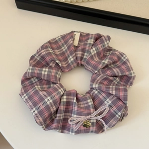 Detail view of plaid scrunchie with pink bow and golden flower pendant featuring handmade tag