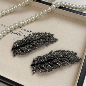 Macro detail of rhinestone-studded leaf hair clips on elegant white fabric lining