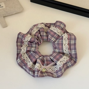 Detailaufnahme von lila kariertem Haargummi mit weißer Spitze, rosa Schleife und Kleeblatt