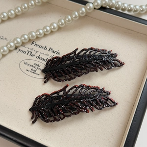 Detailed macro view of rhinestone leaf hair clips with red and black crystals in a jewelry box