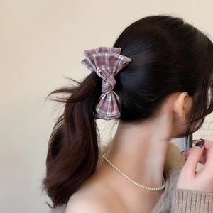 Detailed back view of pink plaid bow hair clip with gold heart emblem on model's ponytail