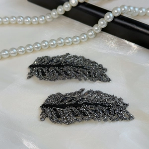 Detailed view of sparkling leaf hair clips with rhinestones on a white silk background