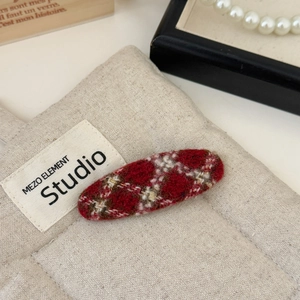 Detailed view of red plaid tweed hair clip with gold thread on quilted fabric background