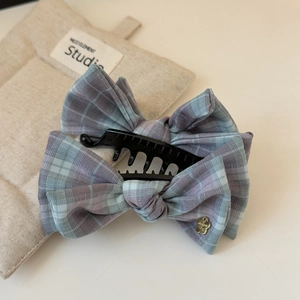 Detail view of blue plaid fabric bow hair clip with gold flower charm on beige mat