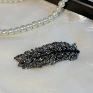 Macro detail of rhinestone leaf hair clip with dark grey crystals on white silk
