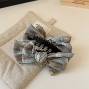 Close-up of brown plaid fabric bow banana clip with gold flower detail on soft mat