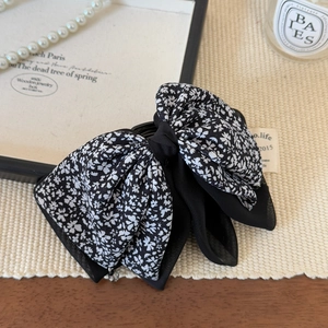 Detail of a double-layered floral bow hair clip with black chiffon on a woven mat