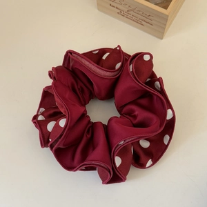 Detail of burgundy satin polka dot scrunchie with soft ruffled texture and silky finish