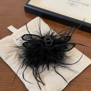 Detail of elegant black feather hair claw clip with mesh wings on beige background