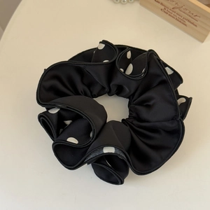 Macro detail of black polka dot scrunchie with soft satin texture and elegant ruffles