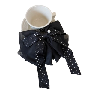 Barrette à cheveux à pois noirs avec perle élégante posée sur une tasse blanche