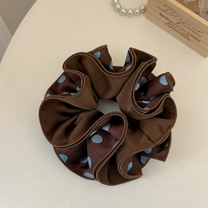 Detail view of large dark brown satin scrunchie with blue polka dots and silk folds