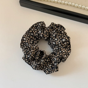 Detail shot of black floral pattern fabric scrunchie with elegant pearl necklace accent
