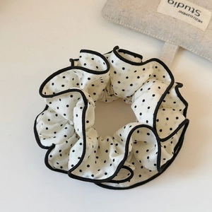 Close-up of cream polka dot scrunchie with black wavy edges and satin texture