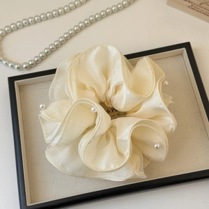 Detail of beige organza oversized scrunchie with pearls on a chic display tray