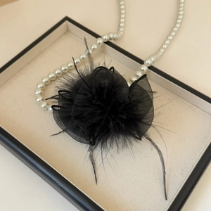 Detailed view of elegant black feather hair clip with mesh petals on a jewelry tray