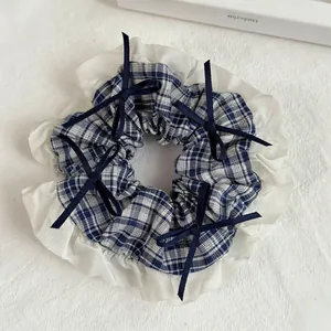 Detail of blue plaid scrunchie with lace trim and navy ribbon bows on fabric background