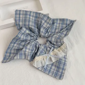 Detail of blue plaid scrunchie featuring white lace trim and a delicate ribbon bow accent