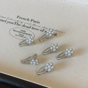 Close-up of 6 silver pearl hair clips with five-petal flower design on a beige board
