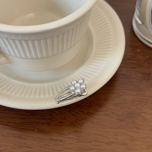 Detail showing a silver flower-shaped pearl hair clip on a white ceramic teacup rim