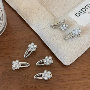 Detailed view of silver duckbill hair clips with pearl flowers on a wooden table