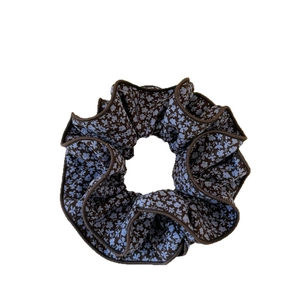 Floral print hair scrunchie with blue blossoms on dark brown fabric with scalloped edges