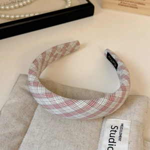 Close-up of pink and white plaid padded headband on beige mat with jewelry decor