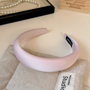 Detail of a light pink satin headband with handmade label on a beige rustic fabric background