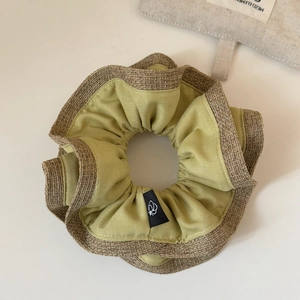 Detail of dual-layer ruffled scrunchie with light green fabric and brown linen textures